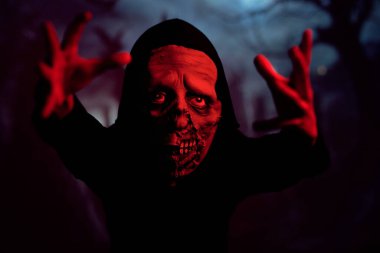 Karanlık mezarlıkta gece vakti parlak kırmızı ışığın altında kameraya uzanan ürkütücü zombi.