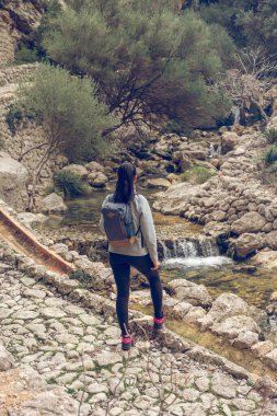 Sırt çantasıyla Mallorca Soller Biniaraix 'i ziyaret ederken kayalık dağlarda akan şelale manzarasının tadını çıkaran kimliği belirsiz kadın gezginin arka planı.
