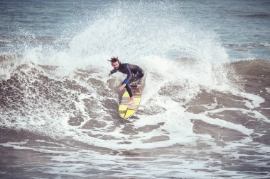 Dalgıç kıyafetli sörfçü adamın tüm vücudu fırtınalı havada köpüklü okyanus dalgalarıyla sörf yapıyor.