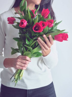 Beyaz arka planda kağıt ambalajda kırmızı lalelerle dikilen, uzun siyah saçlı, tanınmayan bir kadın.