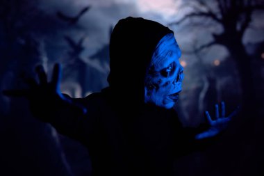 Creepy monster gesticulating and looking away cautiously while sneaking through dark graveyard under blue neon light clipart