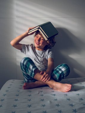 Çıplak ayaklı, gülümseyen ergen bir çocuk. Yatakta oturuyor ve kitap okuyor. Gün ışığında evin çatısına kitap koyuyor.