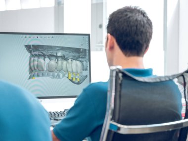 Modern klinikte koltukta oturan tanınmayan diş teknisyeninin arka planda görüntülenmiş 3D diş modeline bakması.
