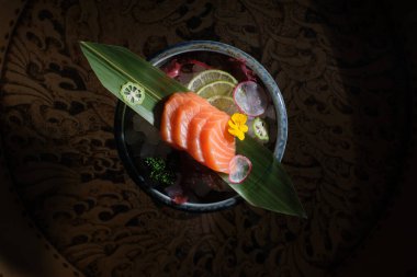 Top view of fresh salmon slices on banana leaf served on bowl with lime slices placed on wooden table in kitchen clipart