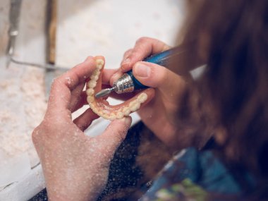 Yukarıdan gelen isimsiz kadın ortodontist, çıkartılamayan takma dişleri parlatırken döner makine kullanıyor.