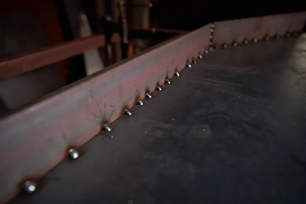 修理作業中の特別な機器とプロの軽作業場で様々なラウンドシームと汚れたテーブルの上に溶接された長い金属片 — ストック写真