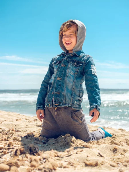Bambino Allegro Giacca Jeans Con Cappuccio Seduto Sulla Costa Sabbiosa — Foto Stock