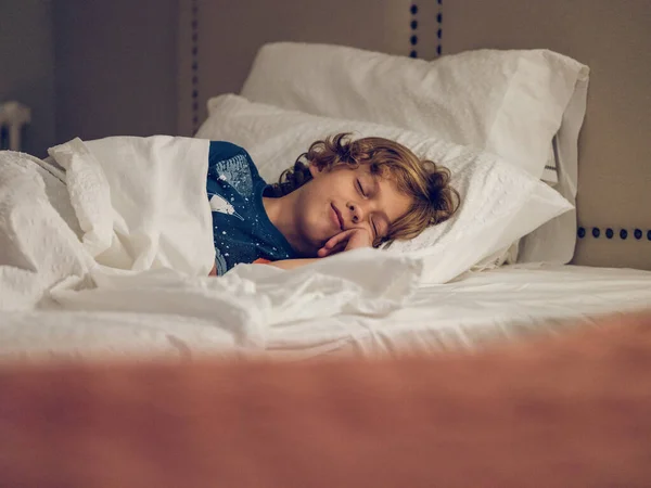 Blond Kid Curly Hair Touching Cheek Lying Soft Bed While — Stock Photo, Image