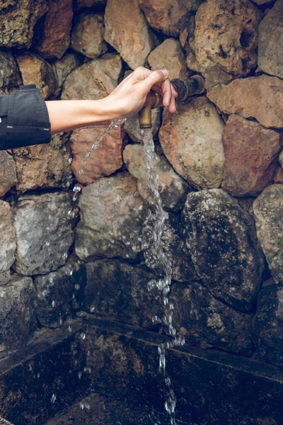 在白天打开纯净矿泉水的同时 无脸女人在旧石墙上拉着铜水龙头 — 图库照片