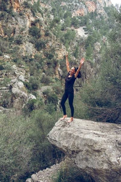 在西班牙马略卡岛的一个夏日 穿着休闲装 光着脚 站在石头上 欣赏群山时 微笑着 挥动着胳膊的快乐女性 — 图库照片