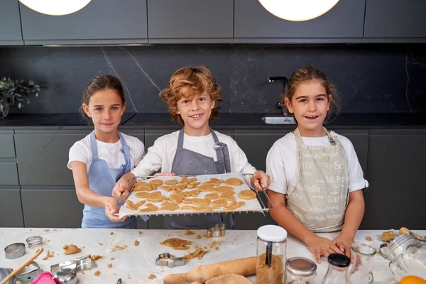 Positive Children Aprons Looking Camera While Showing Baking Tray Sweet — Stock Photo, Image