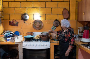 A senior mexican woman is preparing red chili sauce to go with battered poblano chiles using a gas stove. Concept of mexican traditional cooking