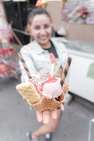A young Hispanic woman is smiling holding a traditional ice cream in front of a street market stall. Concept of traditional Mexican dessert