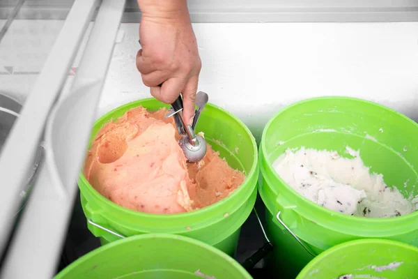 An Hispanic adult woman is taking mamey ice cream with a spoon from a bucket. Close up. Concept of traditional Mexican dessert