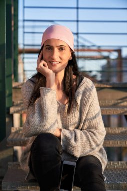 Uzun siyah saçlı, kendine güveni tam bir etnik kadın. Sıradan kıyafetler ve pembe bandana takıyor. Gülümsüyor ve kameraya bakıyor.