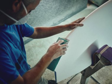 Sörf tahtasının kenarlarını ezen isimsiz erkek üstat atölyedeki profesyonel yıpratıcı ekipmanlarla dolu.