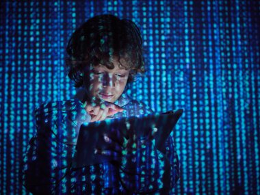 Genç çocuk elinde kod sembolleriyle karanlık odada dikilirken hacklemeye başlamak için tabletteki düğmeye basıyor