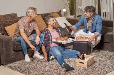 Neşeli olgun erkekler parti sırasında evde pizza ve bira içiyorlar.