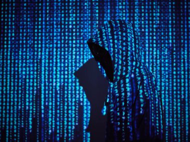 Kapüşonlu anonim hackerın yan görüntüsü loş ışık odasında mavi projeksiyonlu programlama kodu.