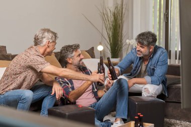 Orta yaşlı erkekler bira içerken ve evde dinlenirken birlikte eğleniyorlar.