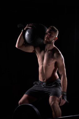 Güçlü kaslı erkek atlet vücut geliştirme egzersizi yaparken omuzundan ağır ağırlık kaldırıyor.