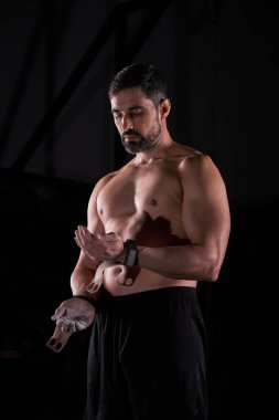 Kas sakallı, bileklikli, elleri tebeşir tozuyla kaplı erkek sporcu siyah arka planda antrenmana hazırlanıyor.