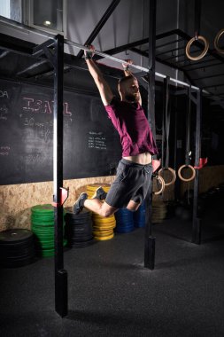 Spor salonunda spor salonunda ekipmanla barfiks çeken aktif giyimli güçlü bir erkek.