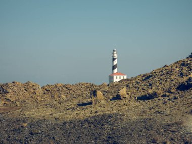 Tepenin tepesindeki deniz feneri kulesinin manzaralı manzarası. Mavi bulutsuz gökyüzünün altındaki dağlık arazi.