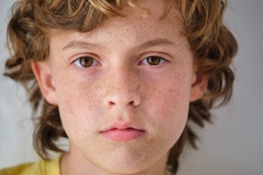 Kahverengi dalgalı saçlı bir çocuğun kameraya bakışıyla ışık arka planına bakması.