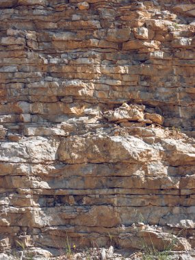 Güneşli bir günde kıraç arazide taş ocağının yaşlanmış, düz olmayan kaya tabakalarıyla kaplı yüzeyi.