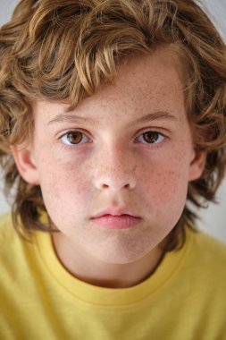 Serious child in yellow casual wear with brown hair and freckles looking at camera clipart