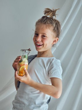 Cam şişeyle kameraya bakan pozitif çocuk turunçgillerden yapılmış lezzetli limonata ve beyaz arka planda nane şekeri ile dolu