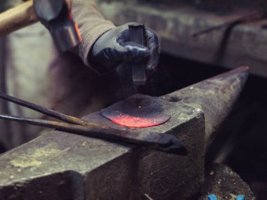 Tanımlanamayan erkek demirci demir dövüyor. Demirhane atölyesinde örse yerleştiriliyor.