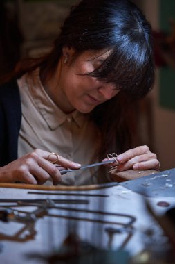 Geleneksel atölyede çalışırken koyu saçlı, mücevherlerin kenarlarını düzleştiren konsantre, etnik kadın kuyumcu.