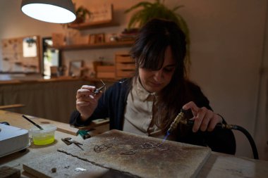 Stüdyoda çalışırken siyah saçlı, meşaleli kuyumcu kadın.