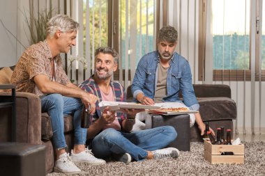 Evde birlikte vakit geçirirken orta yaşlı erkeklerin lezzetli pizzalar yediği bir şirket.