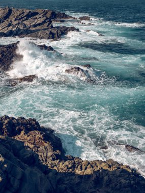 Güneşli bir günde dalgalı kayalıkların yakınından süzülen turkuaz suyla güçlü köpüklü denizin üstünden.