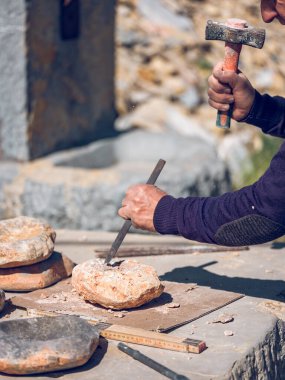 Güneşli bir günde tezgahta taş işçiliği yaparken keski ve çekiç kullanarak taş kesen isimsiz bir zanaatkar.