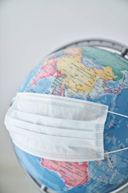 Koronavirüs salgınından korunmak için mavi tıbbi maskeli okyanus ve kıtaların haritası olan renkli plastik küre.
