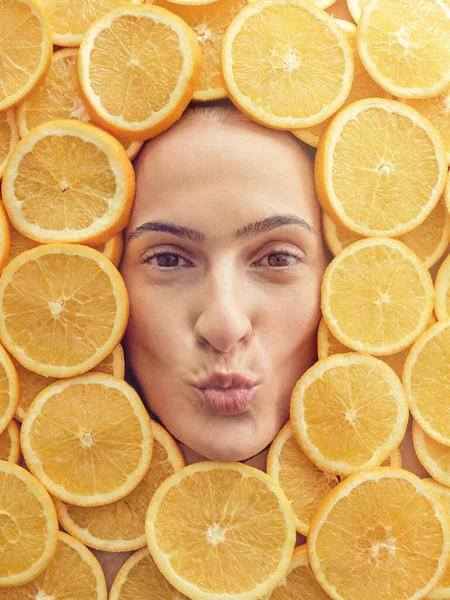 Top view of content brown eyed lady lying in pile of orange slices and making face while looking at camera