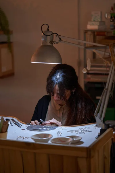 工作室木桌工作时使用旋转钻头时 集中的少数民族女性珠宝商在饰物上创造图案 — 图库照片