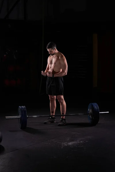 Full body of muscular male athlete preparing for doing deadlift with wrist belt and magnesium