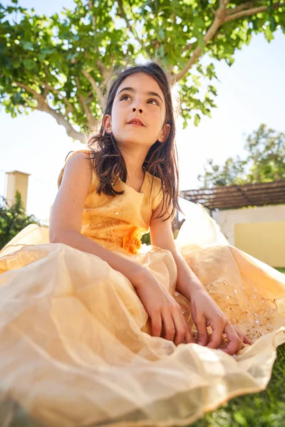 草の芝生の上に座っている黄色のドレスで夢のような子供の低角度と離れて明るい夏の日に緑の裏庭で見る — ストック写真