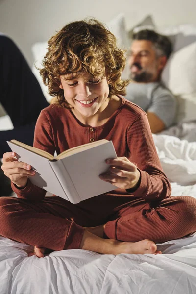 Sonriente Niño Pijama Divirtiéndose Mientras Lee Interesante Libro Contra Padre —  Fotos de Stock