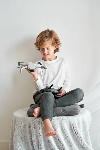Çıplak Ayaklı Çocuk Beyaz Duvarın Karşısında Oturuyor Elinde Oyuncak Drone — Stok fotoğraf