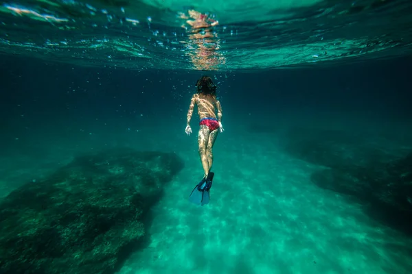 水中で泳いでいるダイビングマスクとスリッパで完全な体の匿名の子供旅行者のバックビュー 美しいサンゴ礁と海底の世界を楽しむ — ストック写真