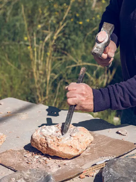 外に石造りの工芸品を作りながら鋭いチゼルとハンマーを使用して固体岩を切断する匿名の職人の上から — ストック写真