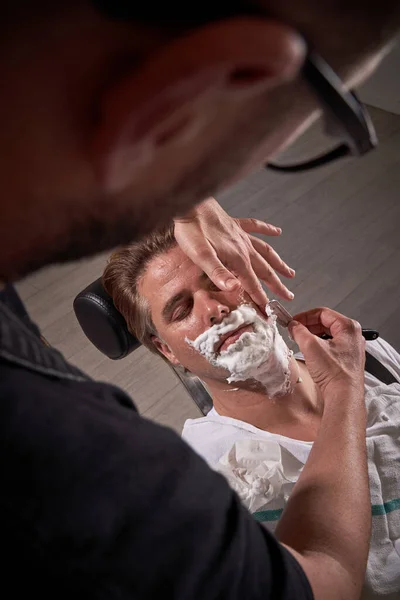 Выше Урожая Анонимный Парикмахер Очках Бритья Бороду Человека Закрытыми Глазами — стоковое фото