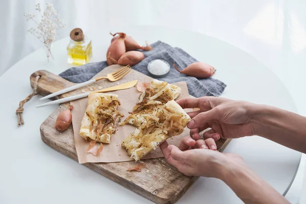 軽い台所の切断板に自家製オニオンタルトを焼いた作物の認識できない人の手の上から — ストック写真