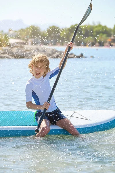 夏休みの間 Supボードに座って波打つ海の水の中でパドルで漕いでいる間に 水着で興奮した子供のフル長さ — ストック写真
